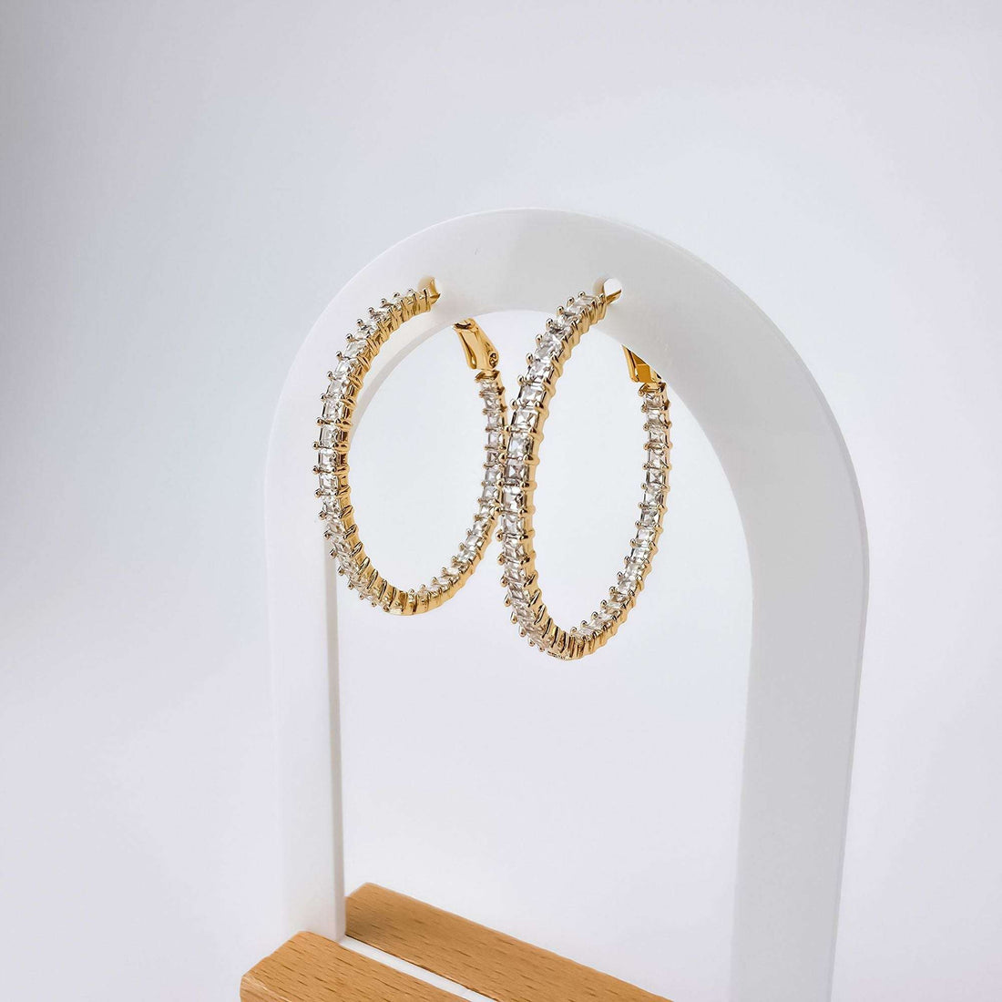 Позолоченные крупные серьги-кольца с квадратными цирконами на белой дугообразной подставке